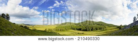 Panoramic mountain summer landscape. Trees near meadow and forest on hillside in sunset light. Diving into the atmosphere.