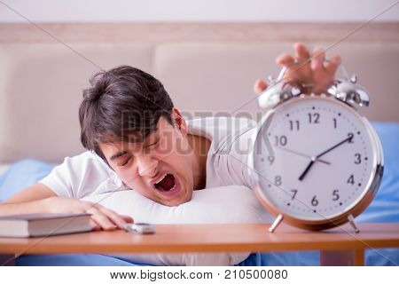 Man in bed frustrated suffering from insomnia with an alarm cloc