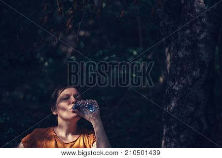 Woman drinking water outdoors. Thirsty adult caucasian female refreshing after long walk through park on sunny summer day unusual framing selective focus