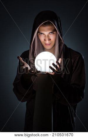 Young wizard with crystal ball in dark room