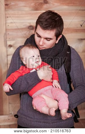 Young father holding son against wooden background. Vertical shot