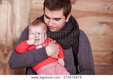 Young father holding son against wooden background. Vertical shot