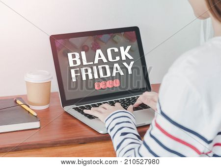 Young Asian woman shopping online with laptop display black Friday screen in home office or co working space.Concept of e-commerce using online technology.