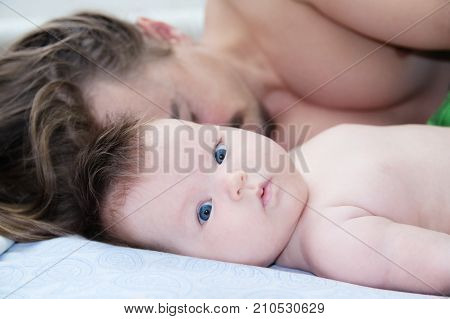 sleeping parent and baby waking up in the morning lying on bed together happy family