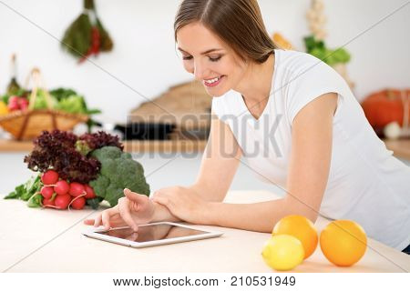 Young woman is making online shopping by tablet computer and credit card. Housewife found new recipe for cooking in a kitchen.