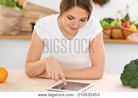 Young woman is making online shopping by tablet computer and credit card. Housewife found new recipe for cooking in a kitchen.