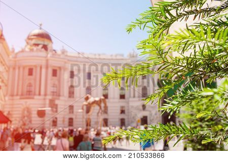 Vienna. Austria. Kohlmarkt street with Hofburg Complex in downtown wtith blurred people and blurred background of a cityscape. Focus on the green leaves.