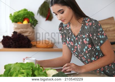 Young hispanic woman is making online shopping by tablet computer and credit card. Housewife found new recipe for cooking in a kitchen.