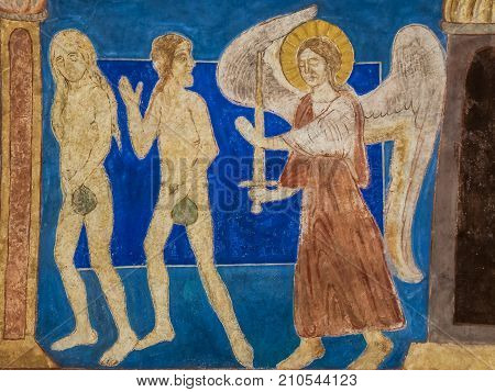 Adam and Eve are expelled from paradise by an angel holding a sword. Medieval mural in Bjaresjo church Sweden November 6 2009