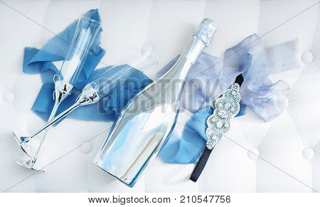 Wedding decorated glasses and platinum champagne bottle on table with silk blue stripes and jewerly