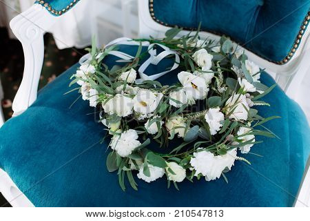 Beautiful wedding circlet lies on vintage blue beige chair. Bouquet consists of white roses, eucalyptus and eustoma.