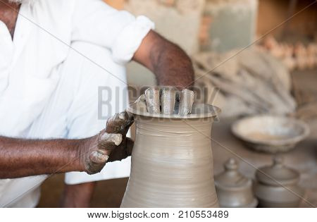 Senior man making handmade clay pottery with bare hands on the potter wheel. India handicrafts