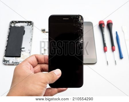 Close-up of cracked smartphone screen in technician hand on blurred smartphone component background