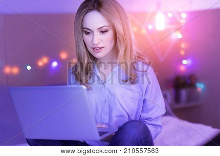Freelancing. Beautiful young concentrated woman sitting at home and looking at the laptop while working on it