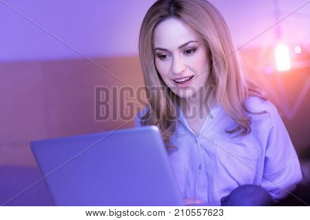 Favourite work. Pretty cheerful young lady working on her laptop and smiling while looking at it