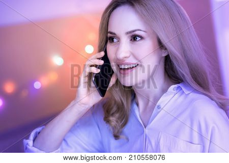Oh wow. Lovely dark-eyed young woman smiling and feeling surprised while talking on the phone
