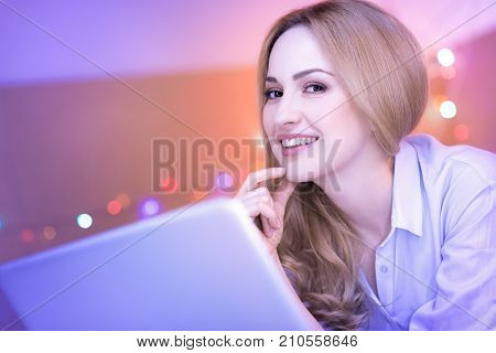 I feel great. Beautiful delighted dark-eyed woman smiling and touching her face while working on the laptop