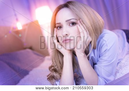 I am sad. Nice sad young lady holding her head with her hands and lying on the sofa being disappointed