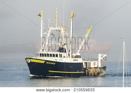 New Bedford Massachusetts USA - October 23 2017: Fishing vessel Monomoy leaving New Bedford harbor on hazy morning with Nantucket Lightship in background
