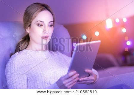 How interesting. Attractive concentrated young woman holding a tablet and reading while sitting