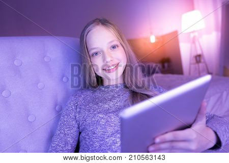 Being inspired. Content blue-eyed blond girl smiling while sitting and using her tablet