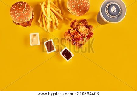 Fast food dish top view. Meat burger, potato chips and chicken. Take away composition. French fries, hamburger, mayonnaise and ketchup sauces on yellow background. Menu or receipt background