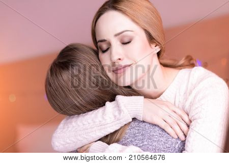 My loved child. Happy loving caring mom hugging her daughter and smiling having her eyes closed
