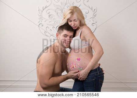 Beautiful pregnant couple in love on the background. Hands of husband on the tummy of his pregnant wife. Young man tenderly stroked pregnant belly of his wife. Husband kissing pregnant belly.