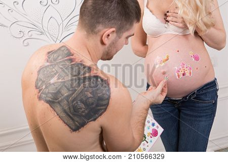 Beautiful pregnant couple in love on the background. Hands of husband on the tummy of his pregnant wife. Young man tenderly stroked pregnant belly of his wife. Husband kissing pregnant belly.