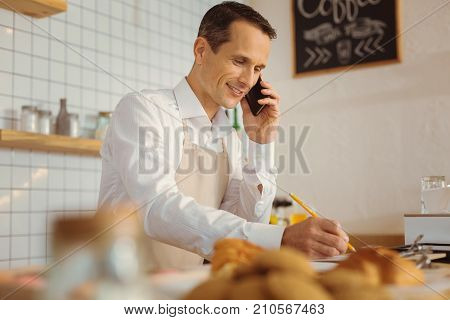 Business issues. Smart nice handsome man making a call and discussing a list of products while taking notes