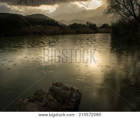 The rain begins to fall, creating patterns on the surface of the river on a still calm day near sunset