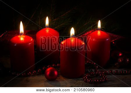 Four red burning candles at the fourth advent christmas decoration with spruce twigs and baubles on a rustic board dark background selective soft focus narrow depth of field