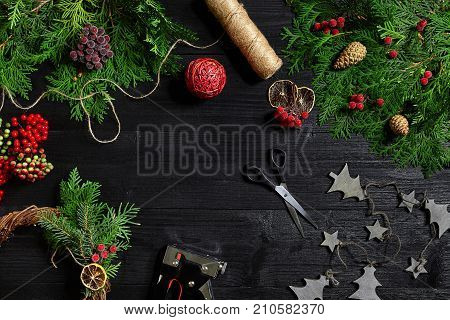 Make a Christmas wreath with your own hands. Spruce branch, Christmas wreath and gifts on a black wooden background. Workplace for preparing handmade decorations.