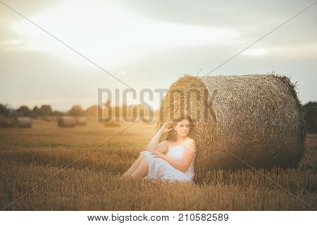Beautiful Girl Sits In A Field With A Bales Of Hay