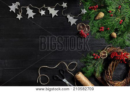 Make a Christmas wreath with your own hands. Spruce branch, Christmas wreath and gifts on a black wooden background. Workplace for preparing handmade decorations.