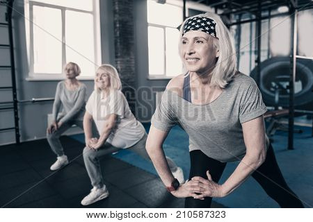 More fun together. Three upbeat elderly women doing stretching while carrying out a warmup before training in gym