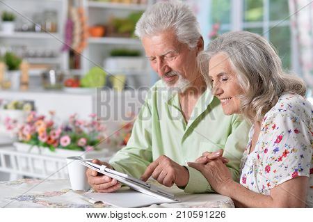 Happy senior couple using digital tablet in kitchen