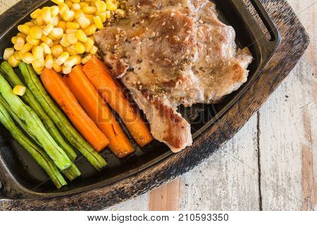 Pork steak with vegetable. Corn carrots green beans on wooden table background.