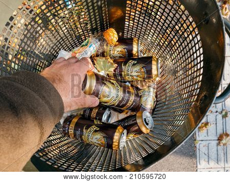STRASBOURG FRANCE - SEP 24 2017: POV Male hand throwing taking Grimbergen beer aluminium can in a public waste bin - homeles concept