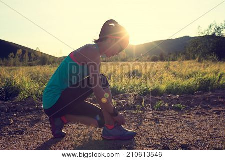 woman runner tying shoelace on forest trail