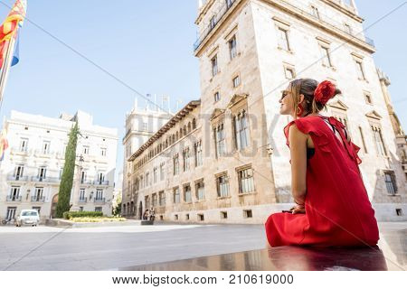 Young woman tourist in red dress sitting on the old town square of Valencia city in Spain