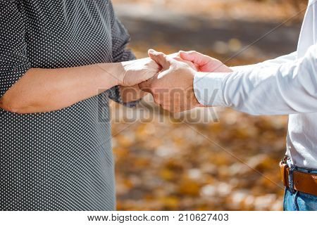 Romantik man and pretty woman holding hands each other on the blurred autumn background. Couple in love walking in the park. Close-up of human hands.
