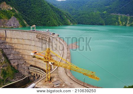 Dam of Inguri hydroelectric power station on the Enguri river with bright blue water on a Sunny day on the background of the Caucasus mountains.