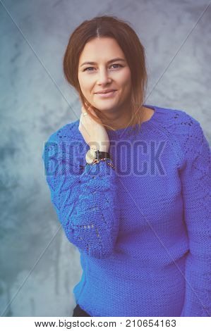Beautiful pregnant woman in a blue knitted self-wearing sweater a black tight skirt posing against a gray unevenly painted wall on city streets on a warm autumn day. Fashion shot of a pregnant woman