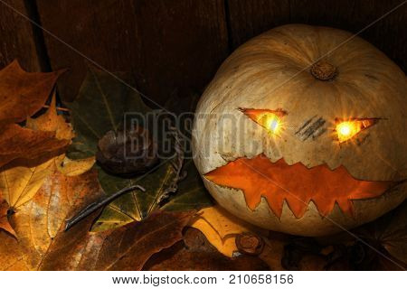 Halloween Jack-o-Lantern with autumn leaves next to a wooden background.