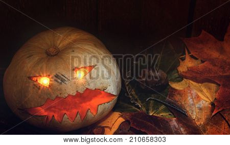 Halloween pumpkin on autumn leaves next to a wooden background