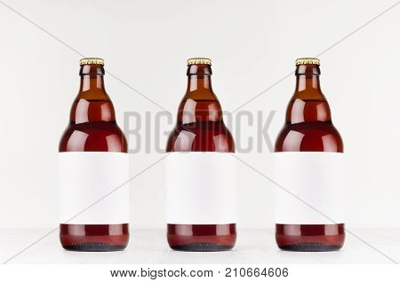 Three brown belgian steinie beer bottles 500ml with blank white label on white wooden board mock up. Template for advertising design branding identity.