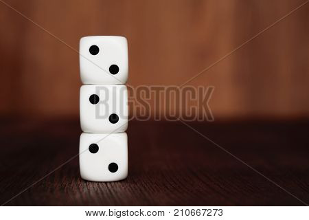 Three white plastic dices on each other on brown wooden board background. Six sides cube with black dots. Number 222.