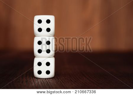 Three white plastic dices on each other on brown wooden board background. Six sides cube with black dots. Number 444.
