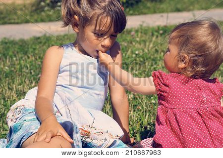 A little girl licks a finger of her younger sister during a picnic on a hot summer day.